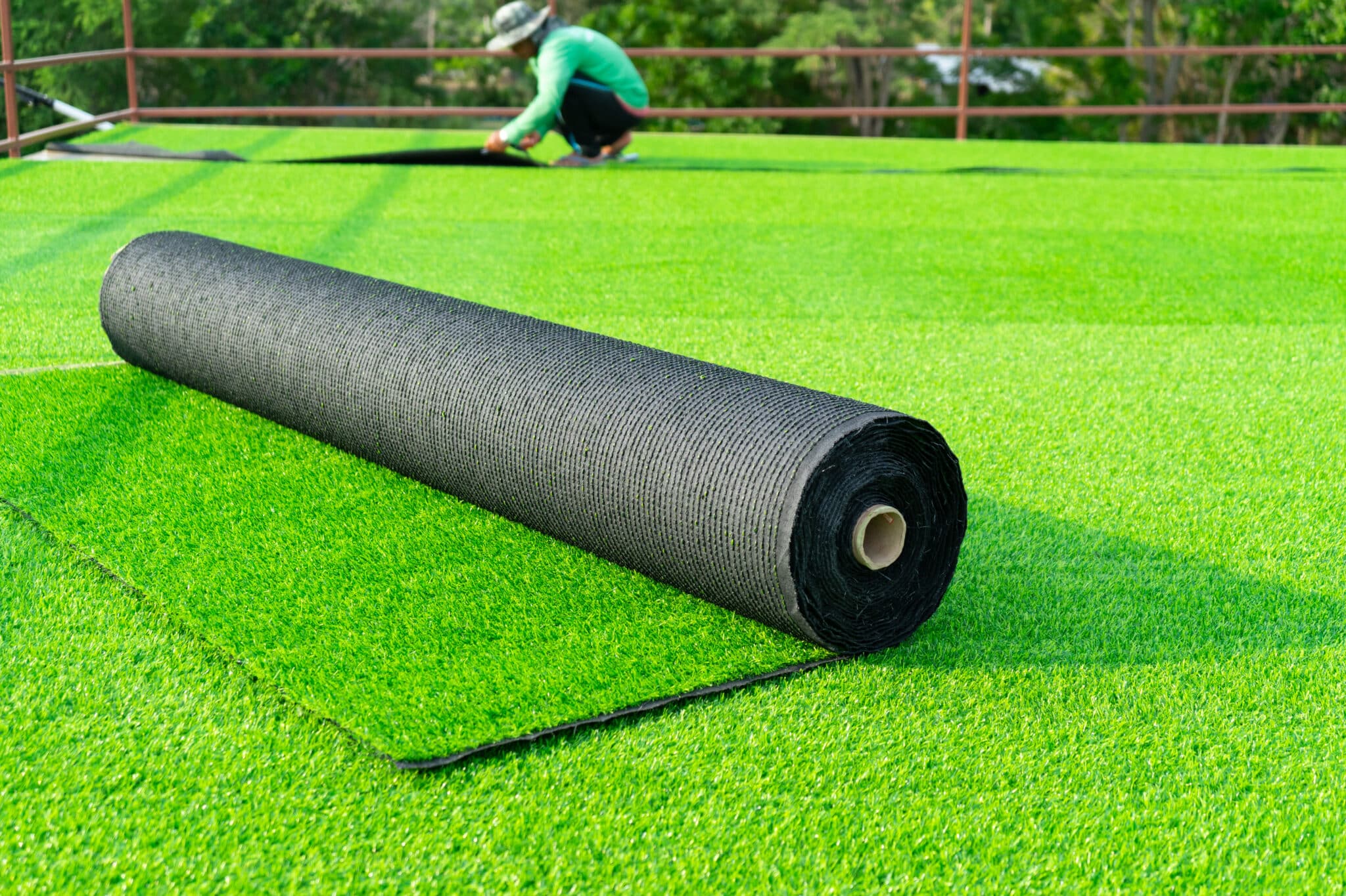 Roll of astroturf or field turf matting of artificial grass soccer field,green lawn background with workers pave the counterfeit grass with sunlight background.
